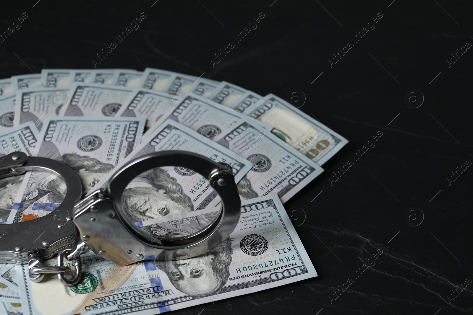 Photo of Corruption. Handcuffs and dollar banknotes on black table, closeup. Space for text