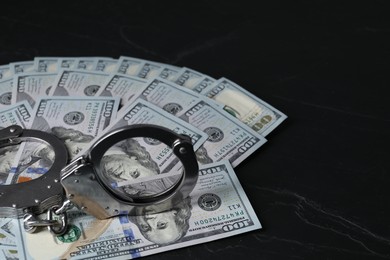 Corruption. Handcuffs and dollar banknotes on black table, closeup. Space for text