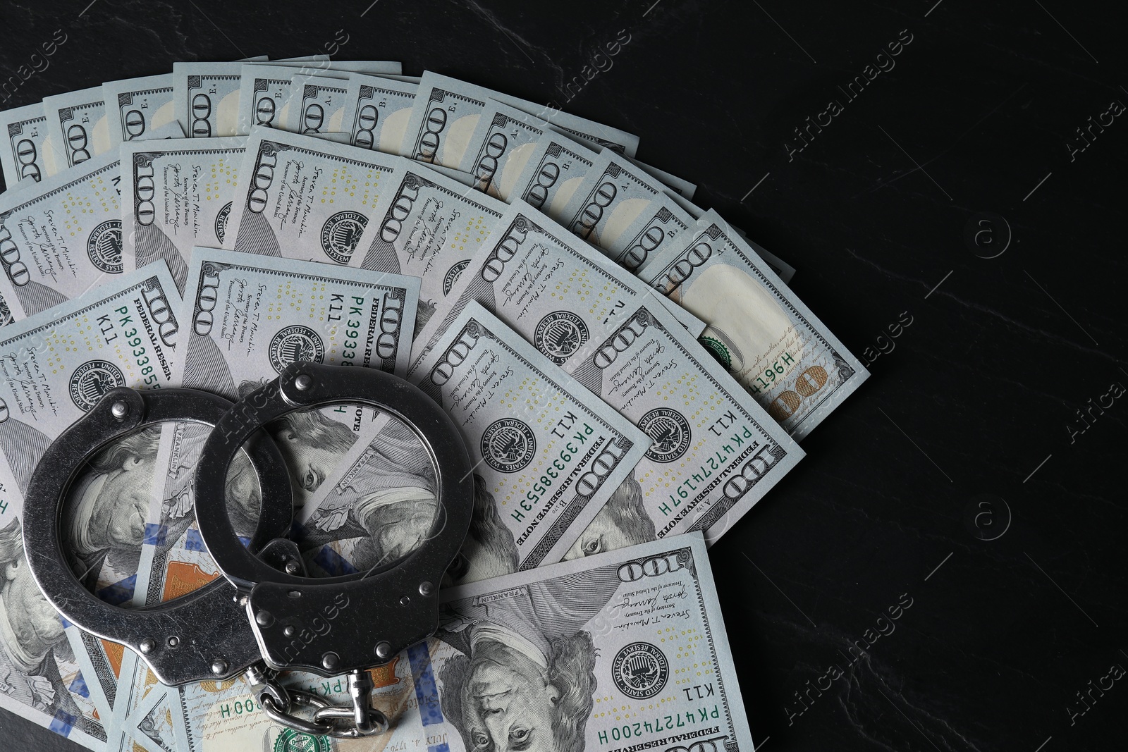 Photo of Corruption. Handcuffs and dollar banknotes on black table, top view