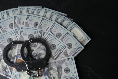 Corruption. Handcuffs and dollar banknotes on black table, top view