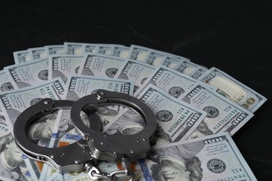 Corruption. Handcuffs and dollar banknotes on black table, closeup