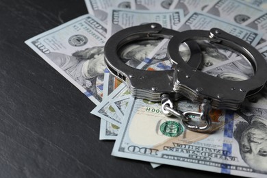 Photo of Corruption. Handcuffs and dollar banknotes on black table, closeup