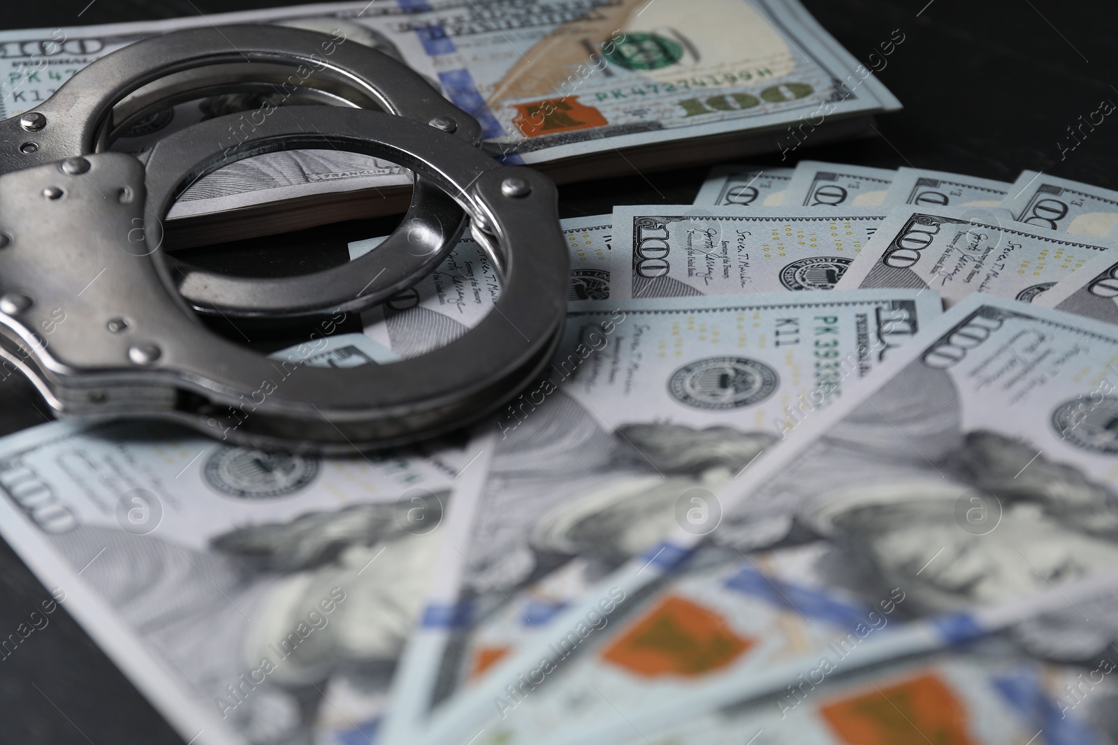 Photo of Corruption. Handcuffs and dollar banknotes on black table, closeup