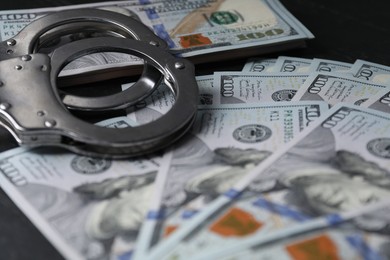 Corruption. Handcuffs and dollar banknotes on black table, closeup