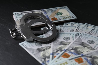 Photo of Corruption. Handcuffs and dollar banknotes on black table, closeup