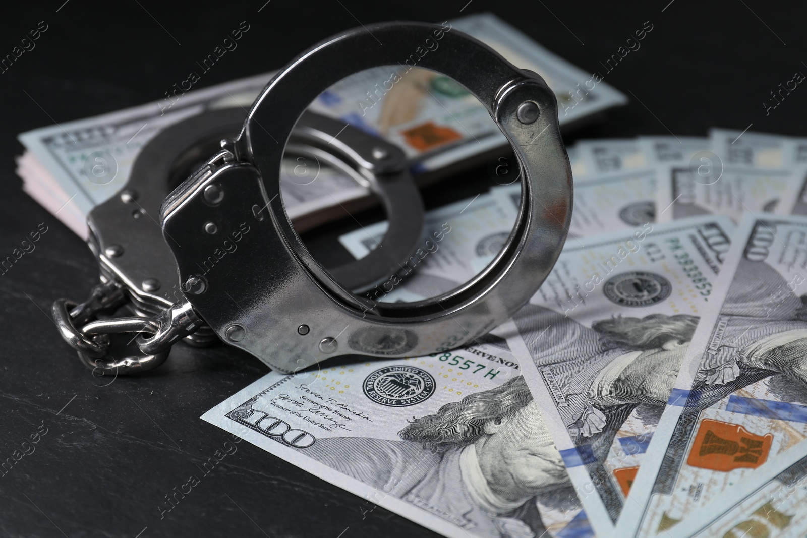 Photo of Corruption. Handcuffs and dollar banknotes on black table, closeup