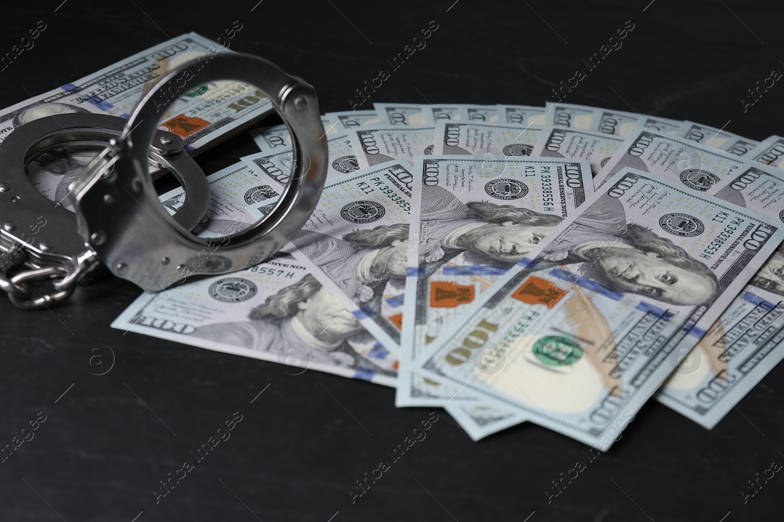 Photo of Corruption. Handcuffs and dollar banknotes on black table, closeup