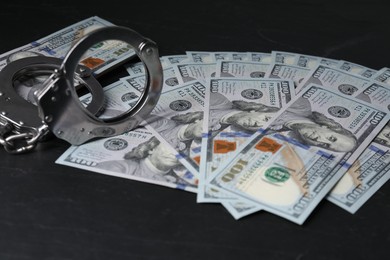 Corruption. Handcuffs and dollar banknotes on black table, closeup