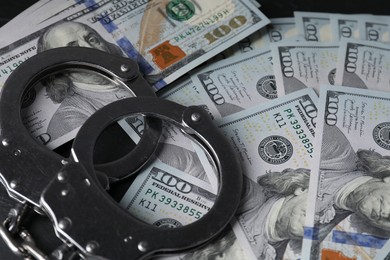 Photo of Corruption. Handcuffs and dollar banknotes on table, closeup