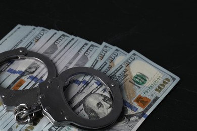 Photo of Corruption. Handcuffs and dollar banknotes on black table, closeup