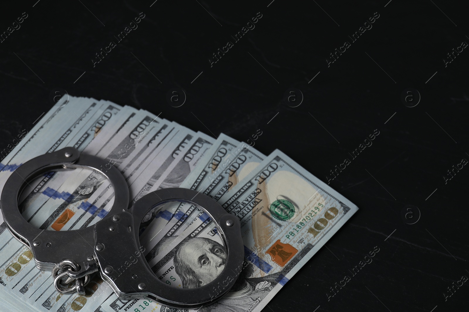 Photo of Corruption. Handcuffs and dollar banknotes on black table, closeup. Space for text