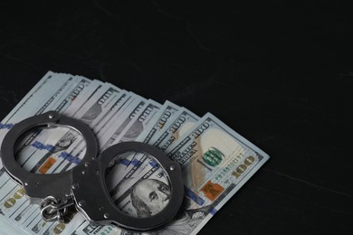 Photo of Corruption. Handcuffs and dollar banknotes on black table, closeup. Space for text