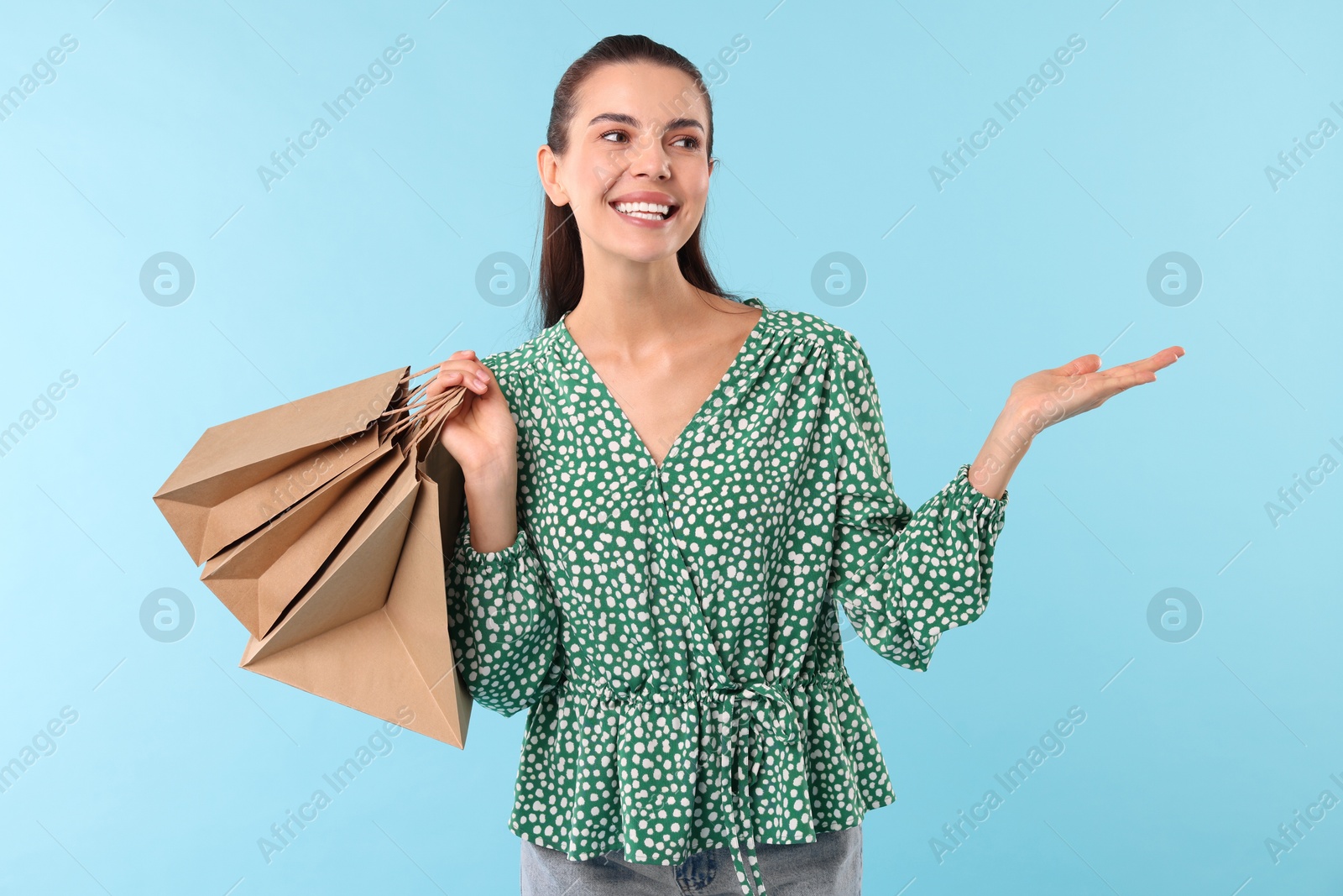 Photo of Smiling woman with shopping bags holding something on light blue background