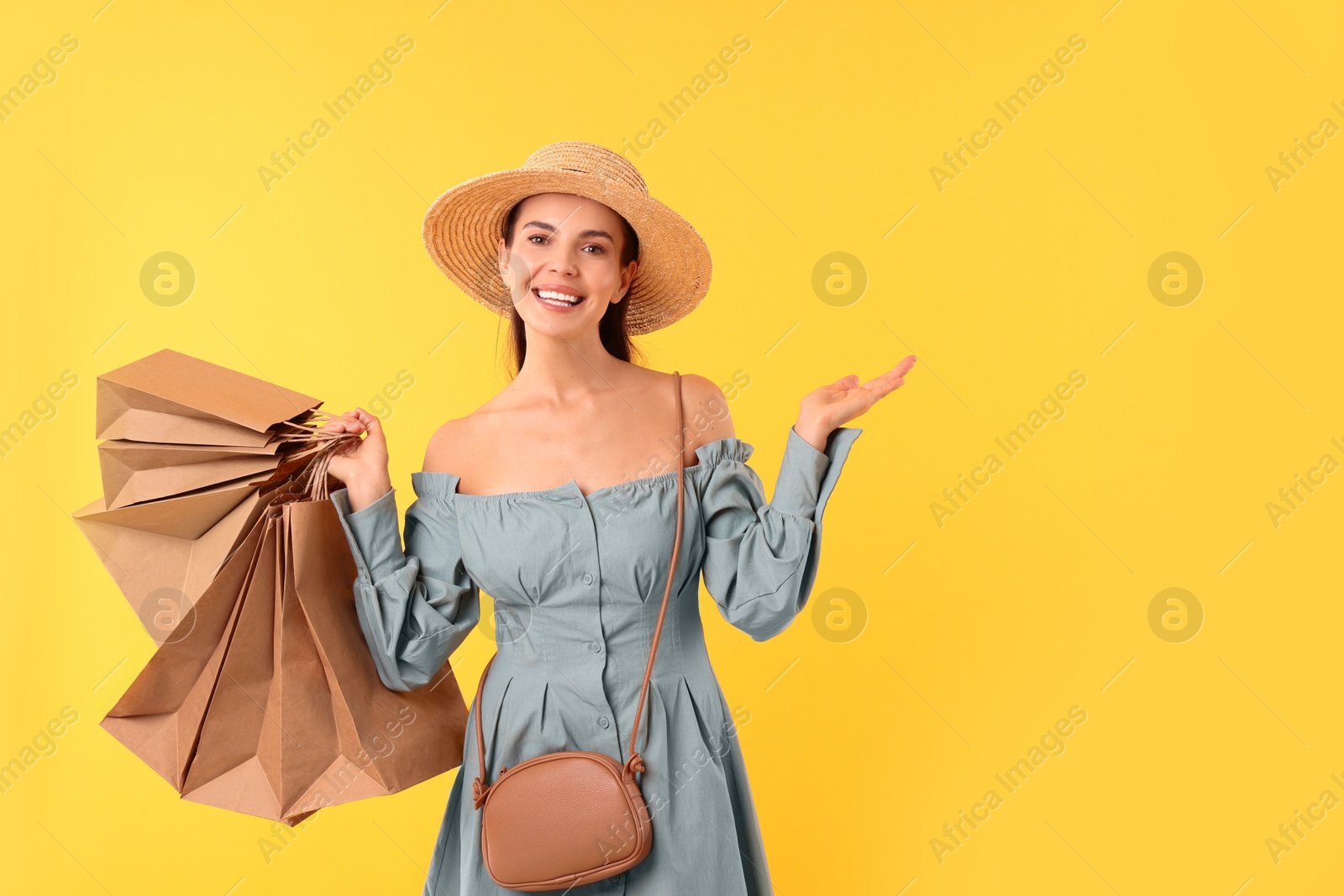 Photo of Smiling woman with shopping bags holding something on yellow background. Space for text