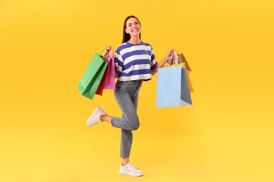 Photo of Smiling woman with colorful shopping bags on yellow background