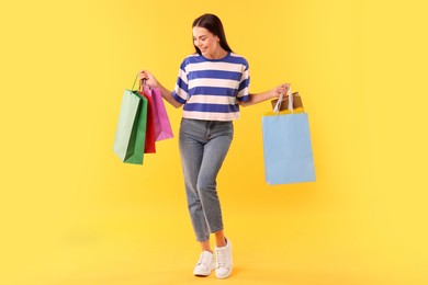 Smiling woman with colorful shopping bags on yellow background