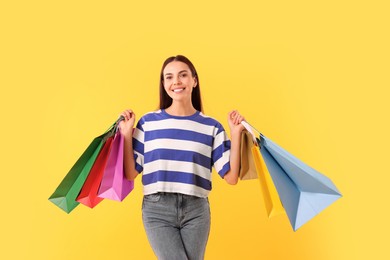 Smiling woman with colorful shopping bags on yellow background