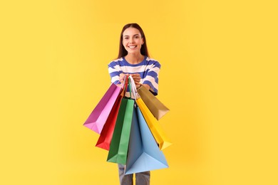 Photo of Smiling woman showing colorful shopping bags on yellow background