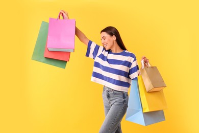 Smiling woman with colorful shopping bags on yellow background