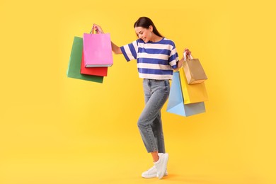 Photo of Smiling woman with colorful shopping bags on yellow background