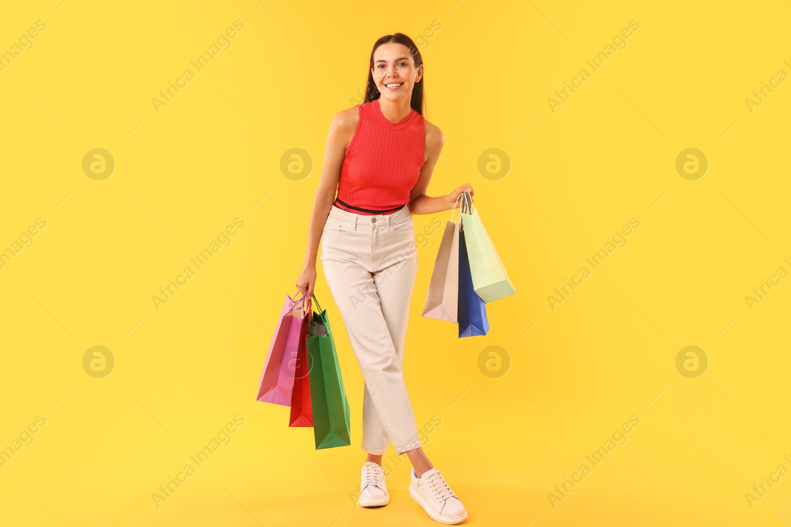 Photo of Smiling woman with colorful shopping bags on yellow background