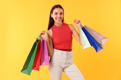 Smiling woman with colorful shopping bags on yellow background