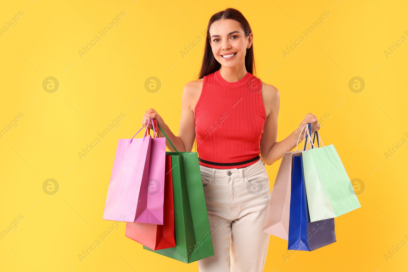 Photo of Smiling woman with colorful shopping bags on yellow background