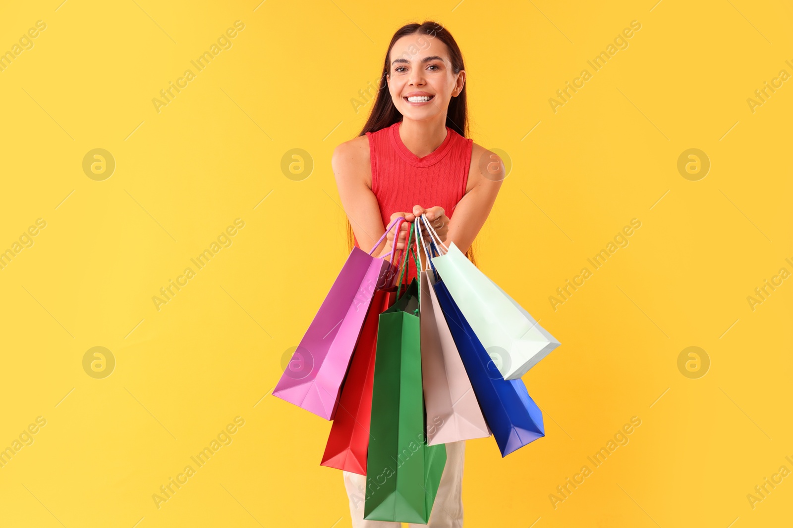 Photo of Smiling woman with colorful shopping bags on yellow background