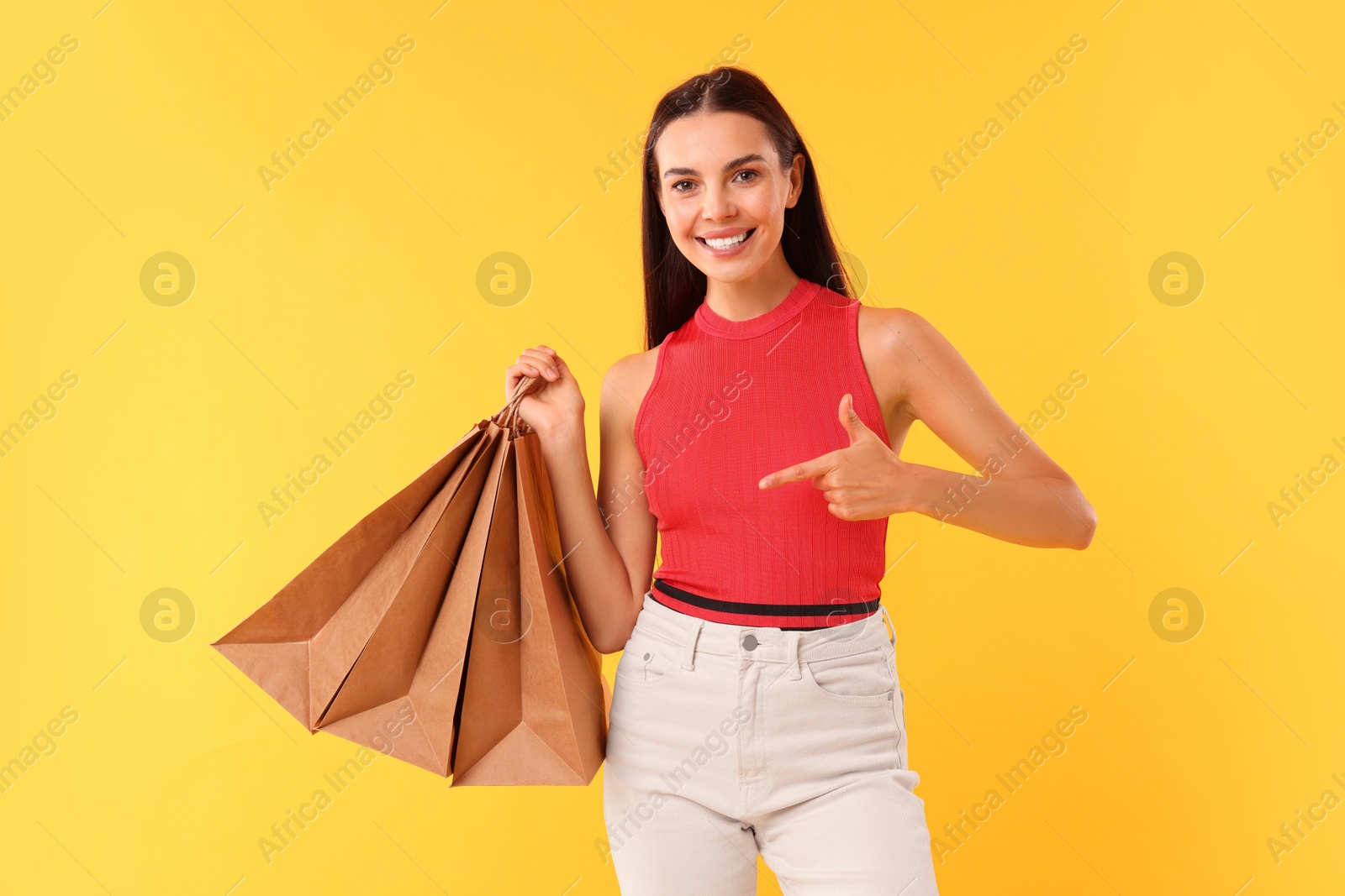 Photo of Smiling woman pointing at shopping bags on yellow background