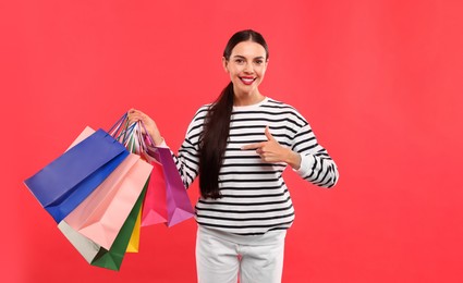 Smiling woman pointing at colorful shopping bags on red background