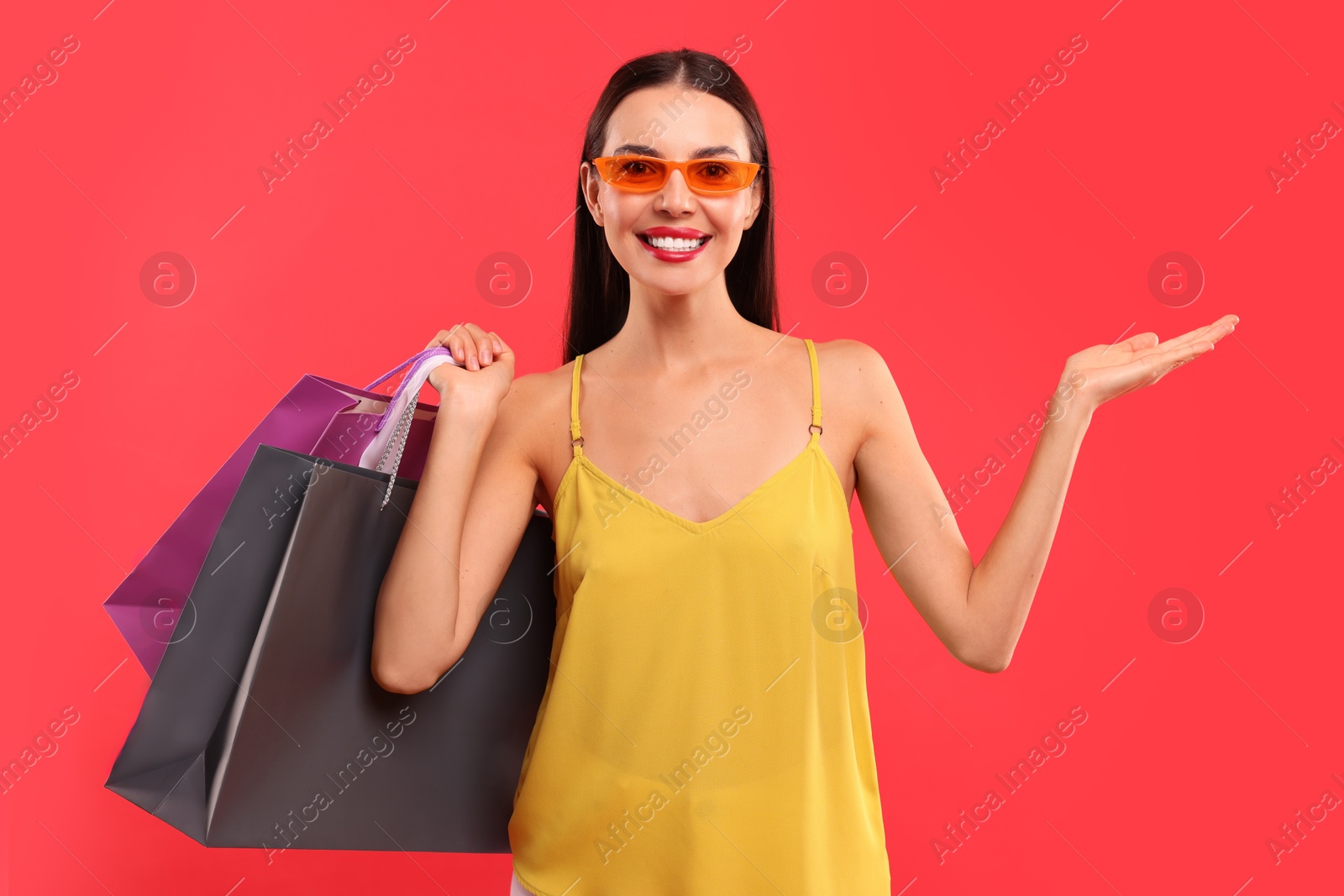 Photo of Smiling woman with colorful shopping bags holding something on red background