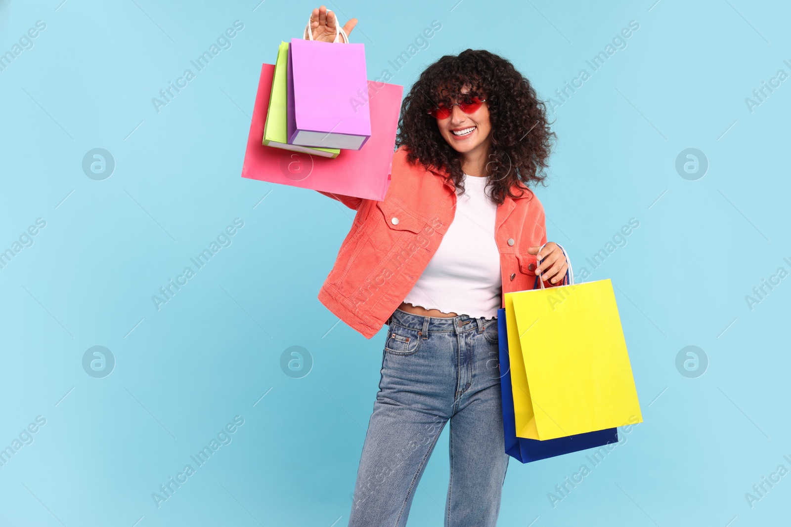 Photo of Smiling woman with colorful shopping bags on light blue background