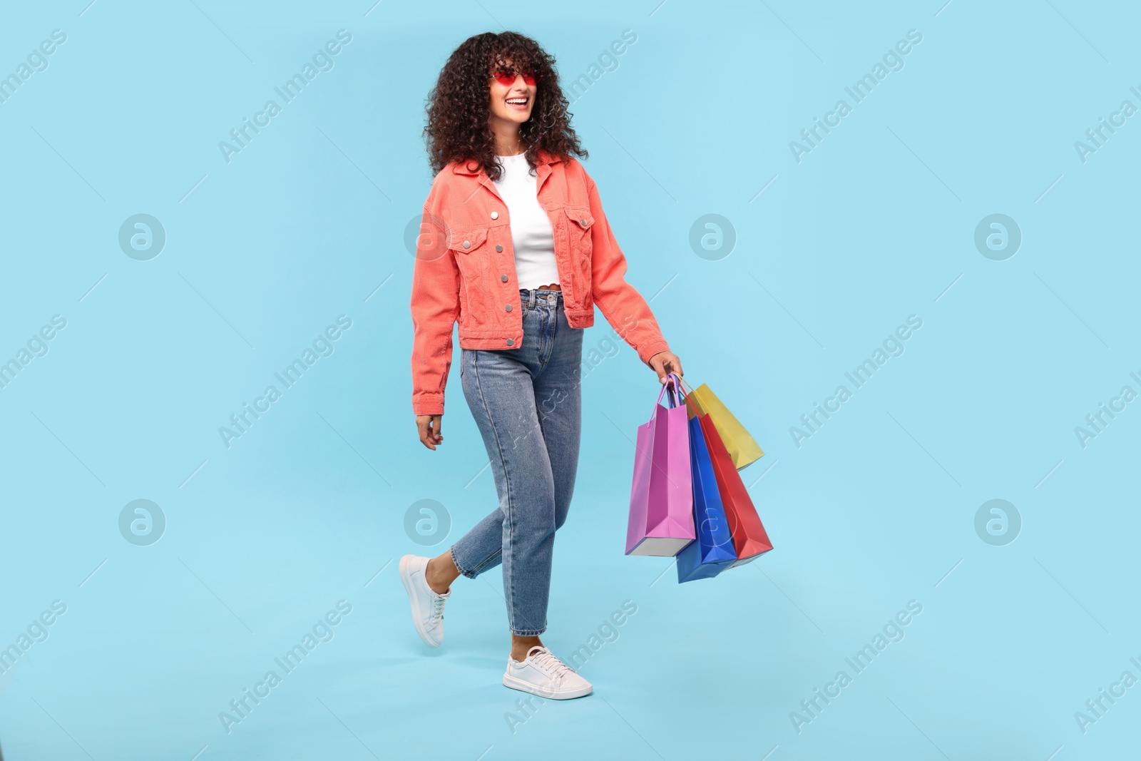 Photo of Smiling woman with colorful shopping bags on light blue background