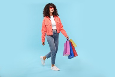 Photo of Smiling woman with colorful shopping bags on light blue background