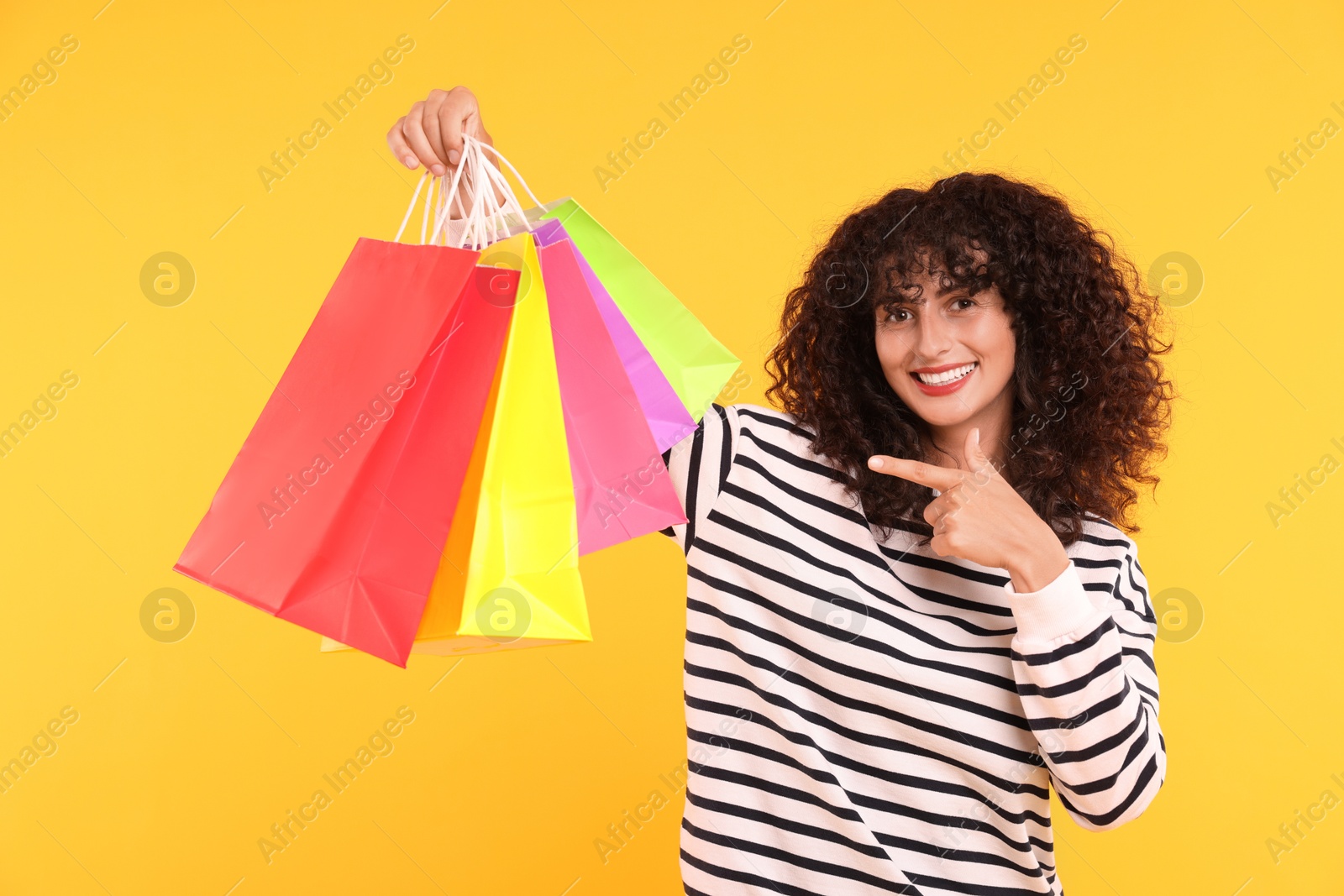 Photo of Smiling woman pointing at colorful shopping bags on yellow background