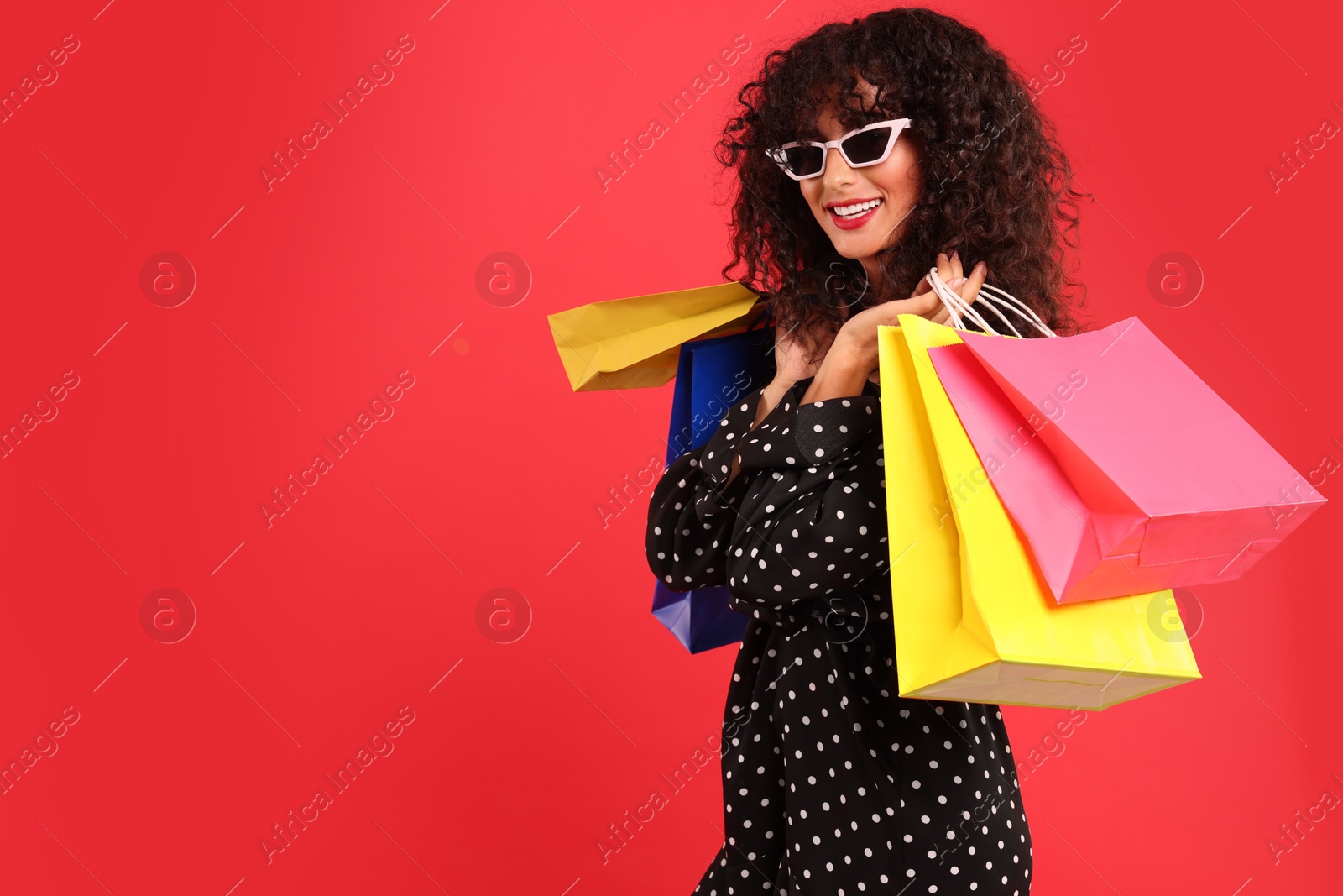 Photo of Smiling woman with colorful shopping bags on red background. Space for text