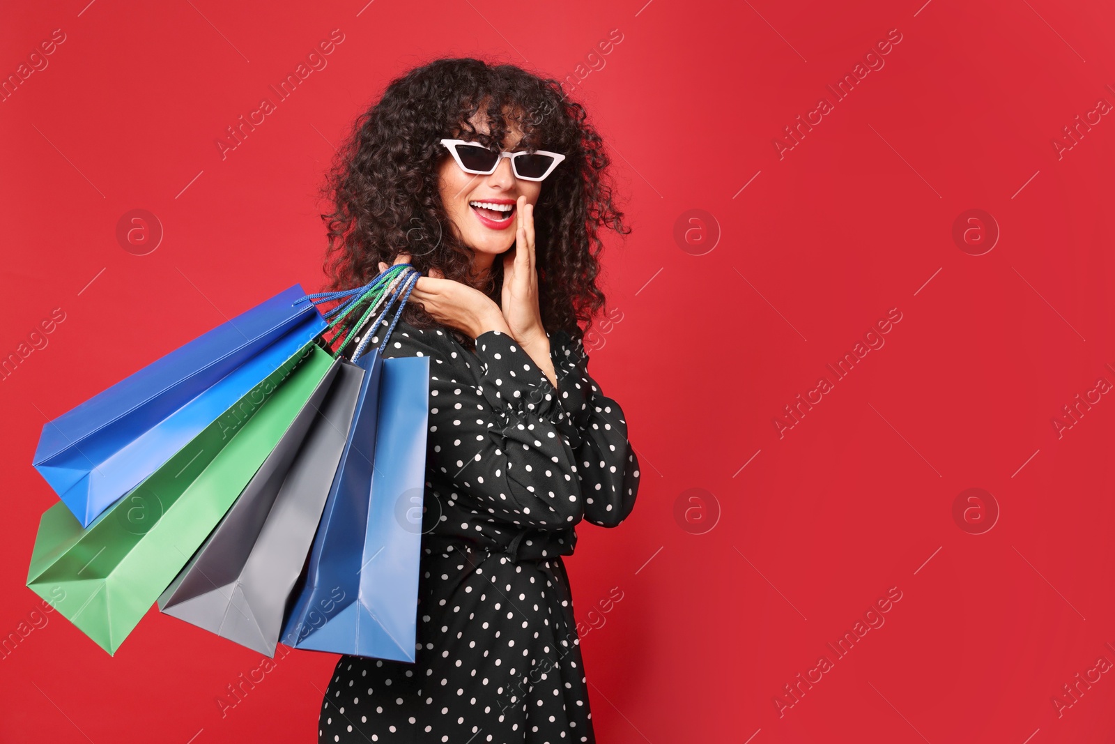 Photo of Happy woman with colorful shopping bags on red background. Space for text