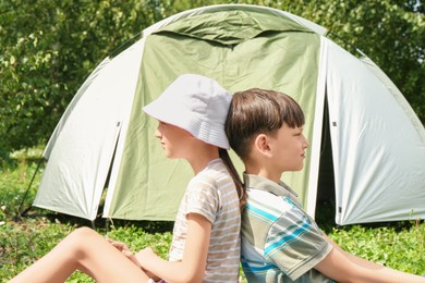 Girl and her brother spending time together near camping tent outdoors