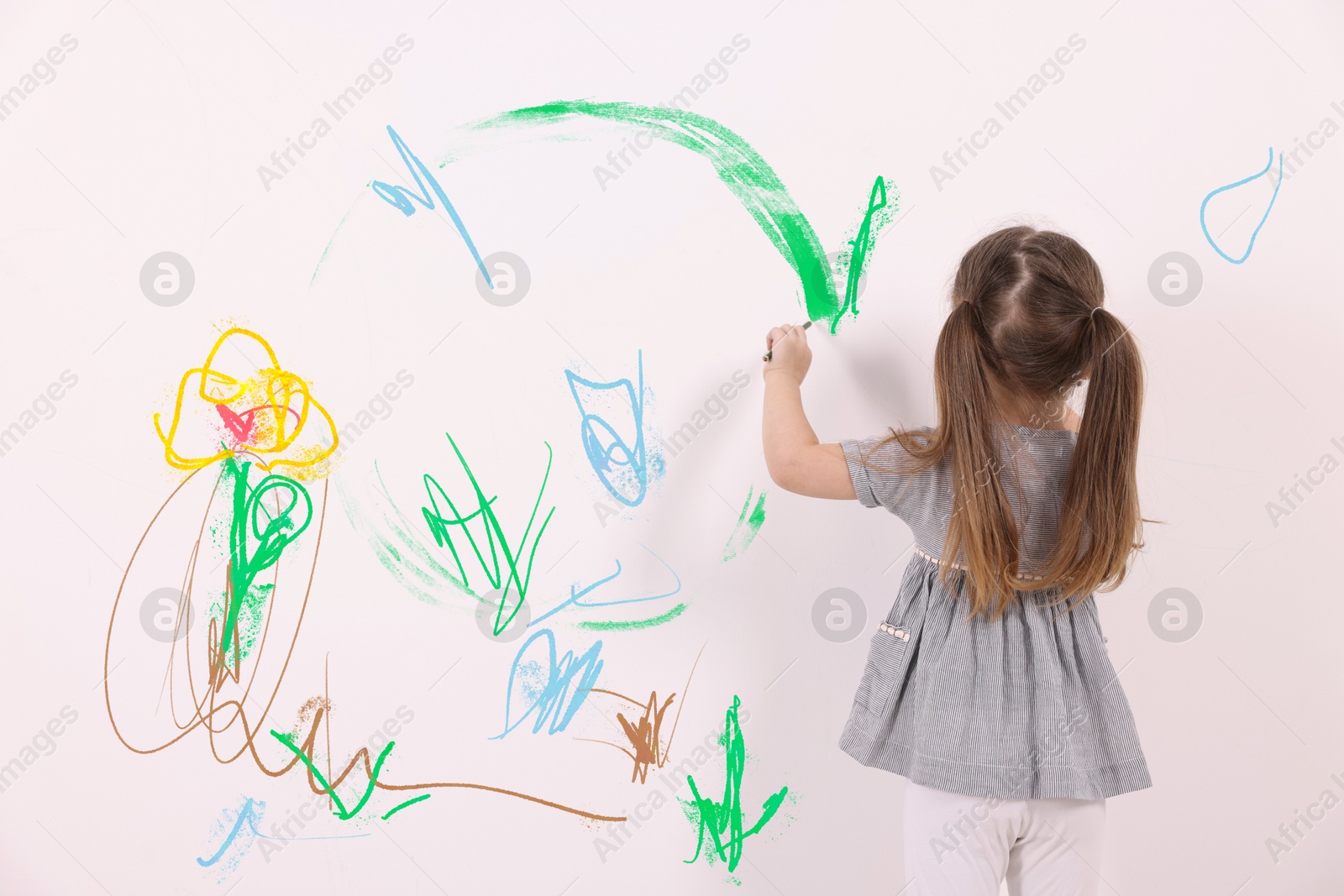 Image of Little child drawing on white wall, back view