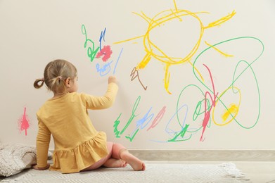 Little child drawing on white wall, back view