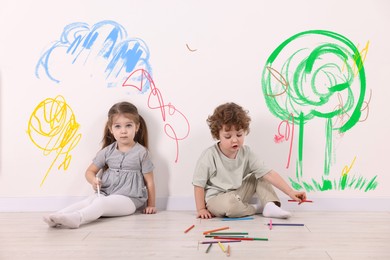 Image of Little children sitting near white wall with drawings