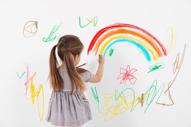 Little child drawing on white wall, back view