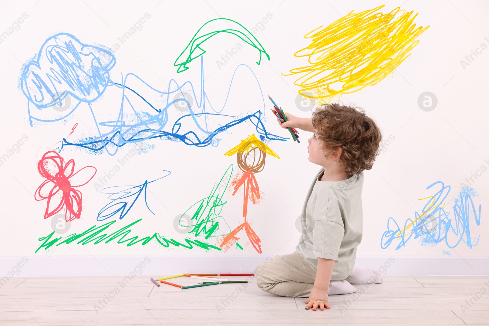 Image of Little child sitting on floor and drawing on white wall