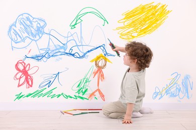 Image of Little child sitting on floor and drawing on white wall