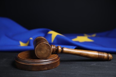 Photo of Judge's gavel and European Union flag on grey table against black background, closeup