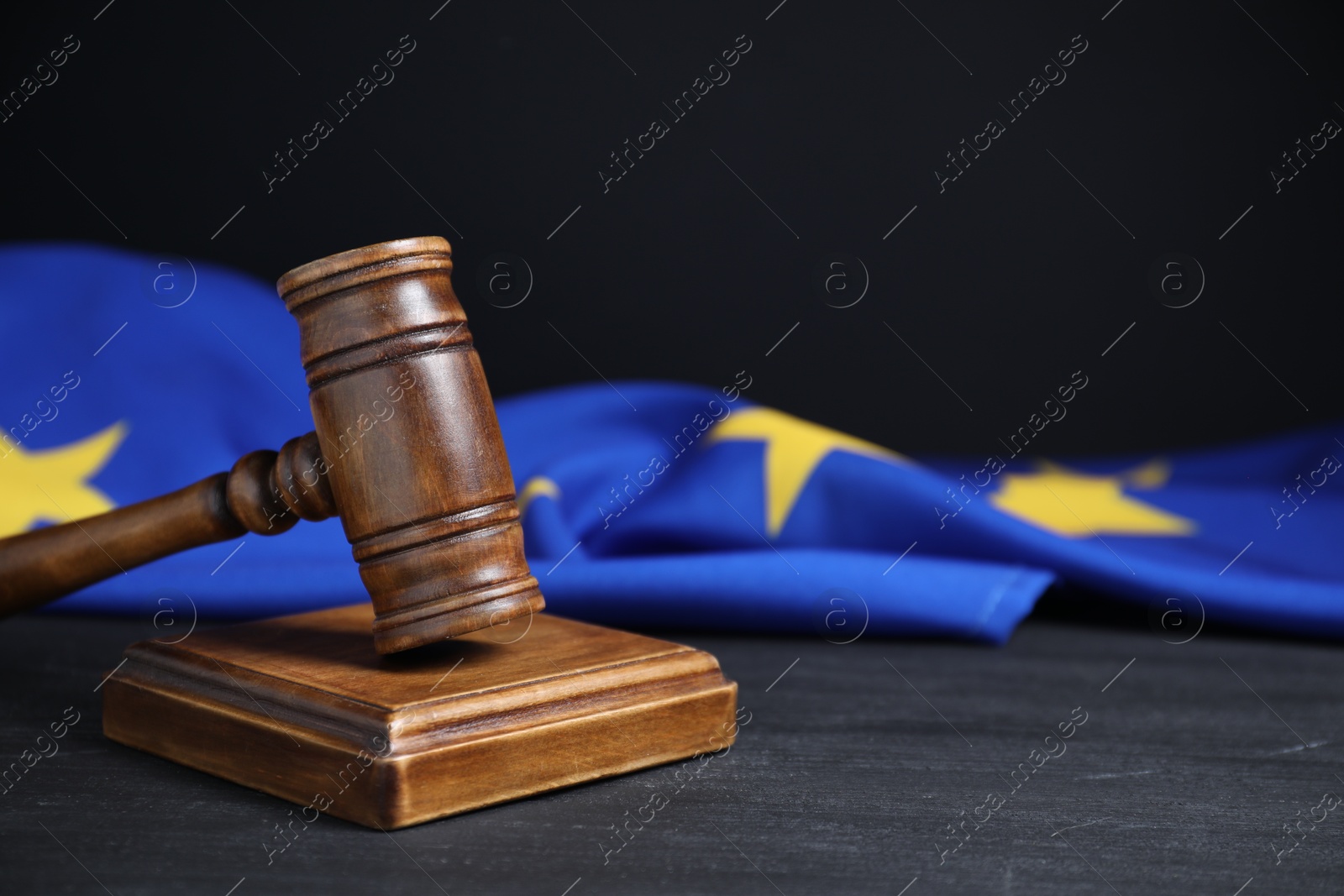 Photo of Judge's gavel and European Union flag on grey table against black background, closeup. Space for text