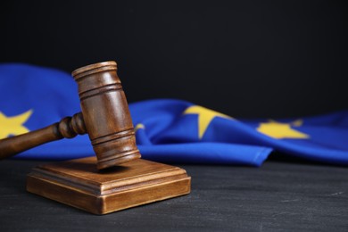 Photo of Judge's gavel and European Union flag on grey table against black background, closeup. Space for text