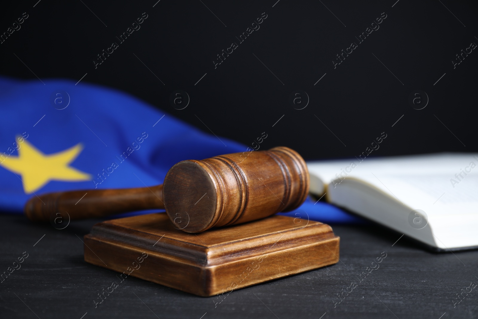 Photo of Judge's gavel, book and European Union flag on grey table against black background, closeup