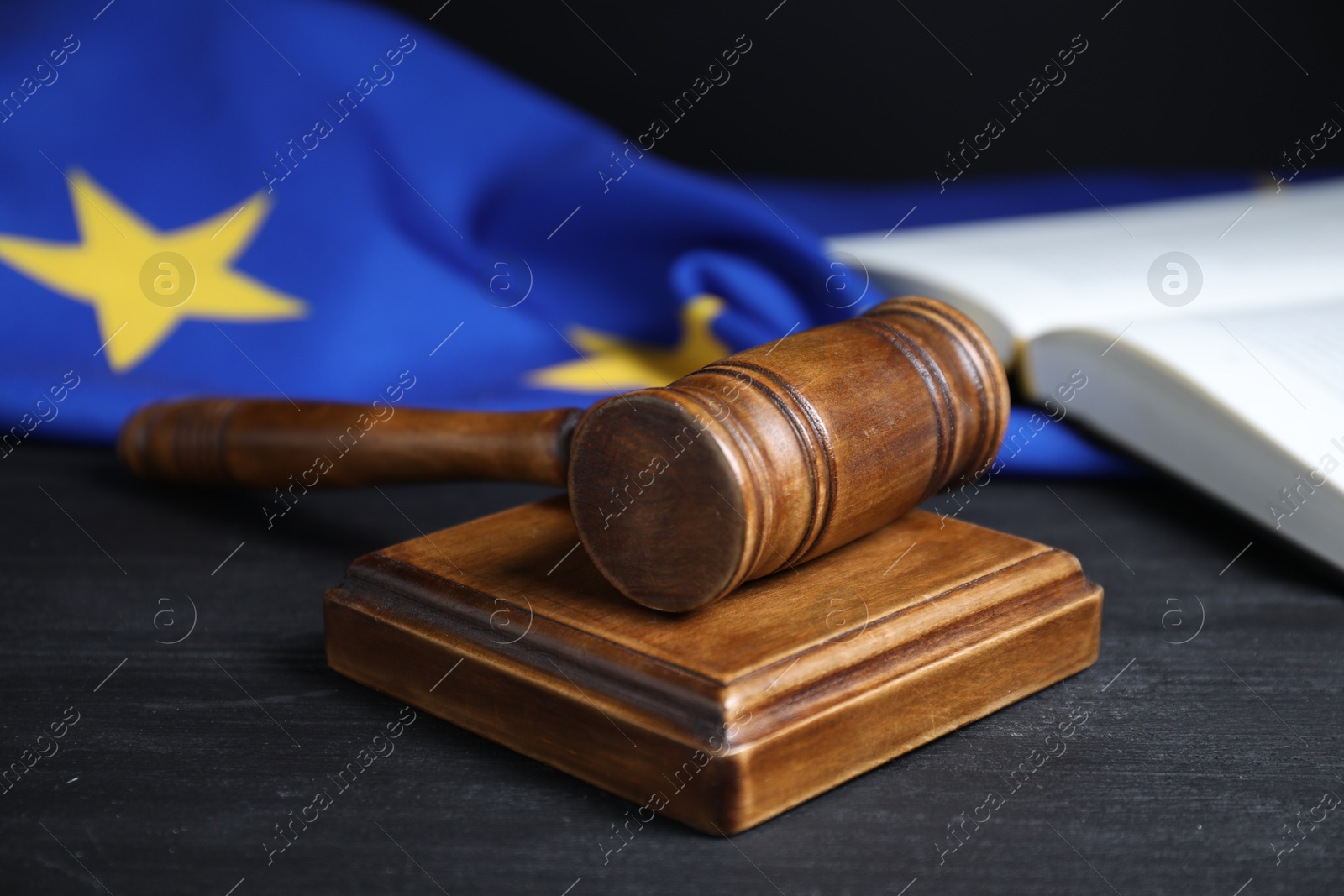 Photo of Judge's gavel, book and European Union flag on grey table against black background, closeup