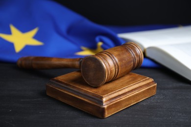 Photo of Judge's gavel, book and European Union flag on grey table against black background, closeup